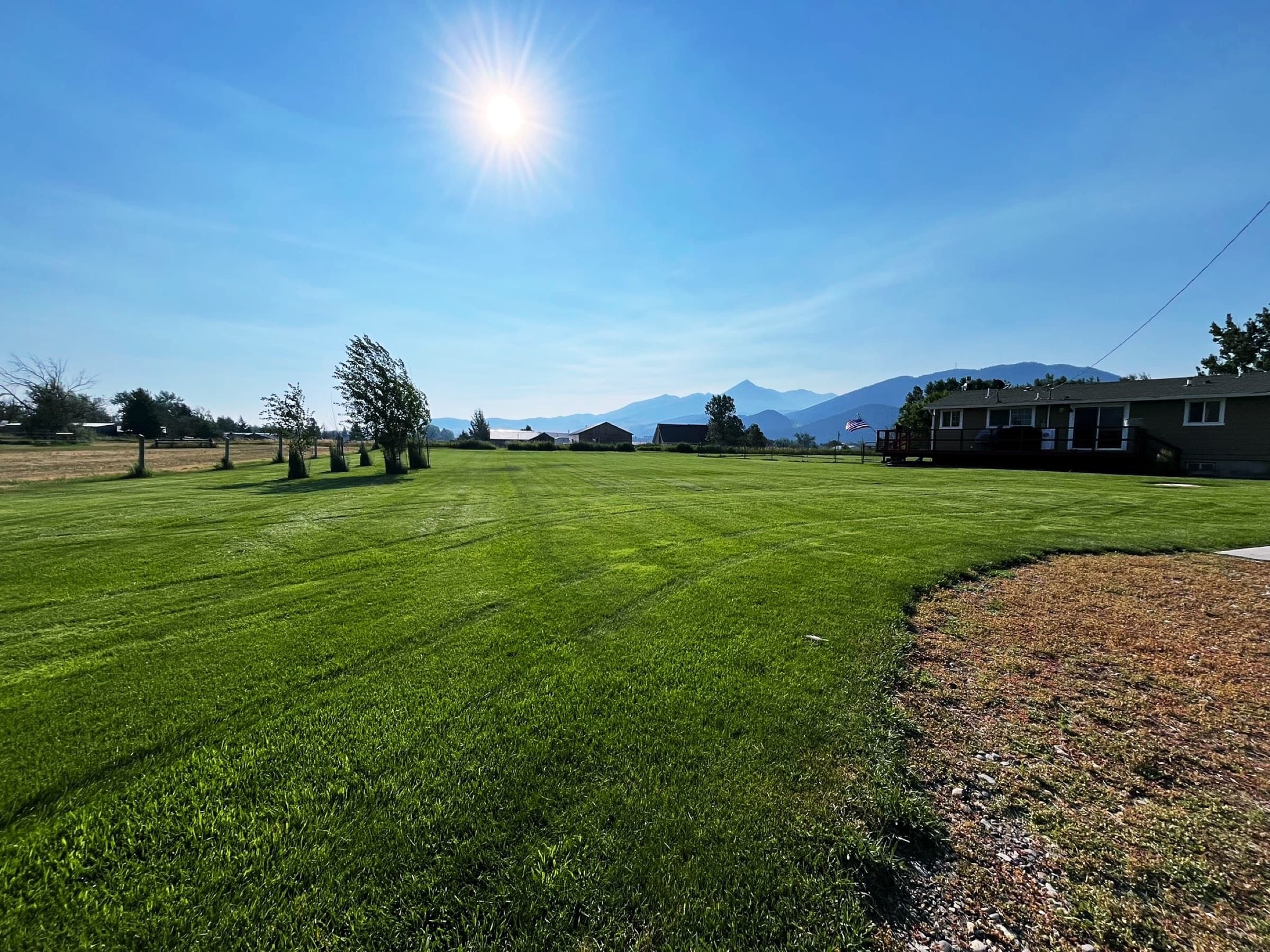 Wide green lawn with a Bozeman-area home, mountain backdrop, and morning sun